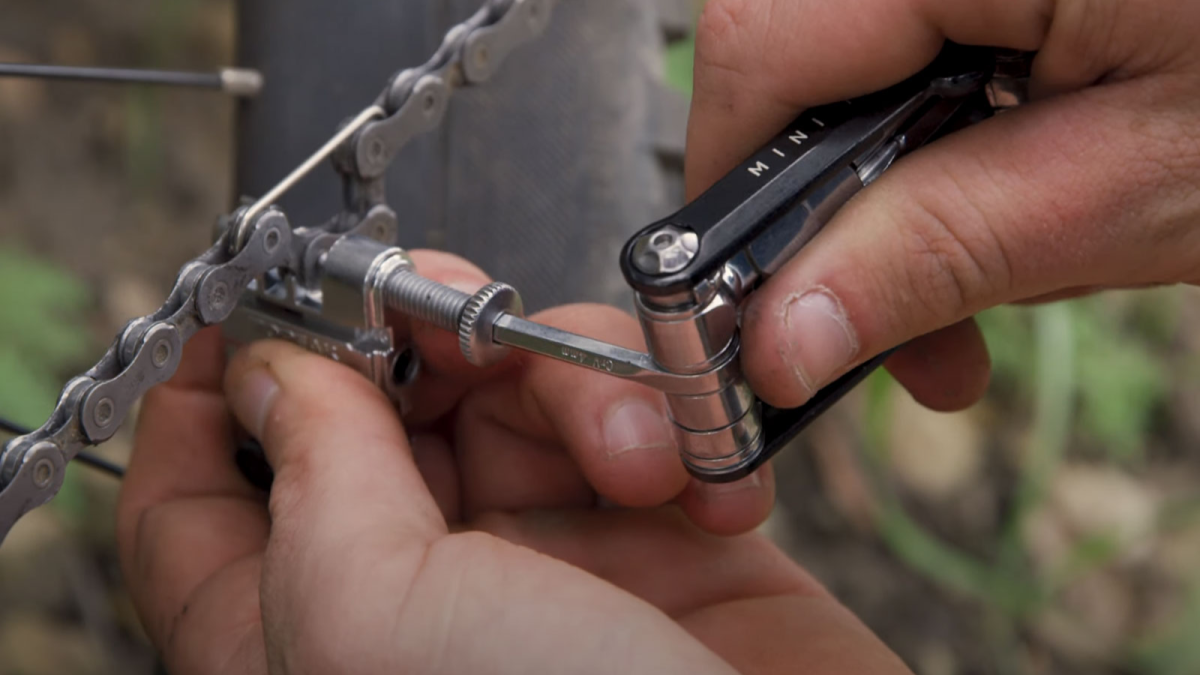 A close up to two hands using a Topeak multi-tool to split a chain on a bike