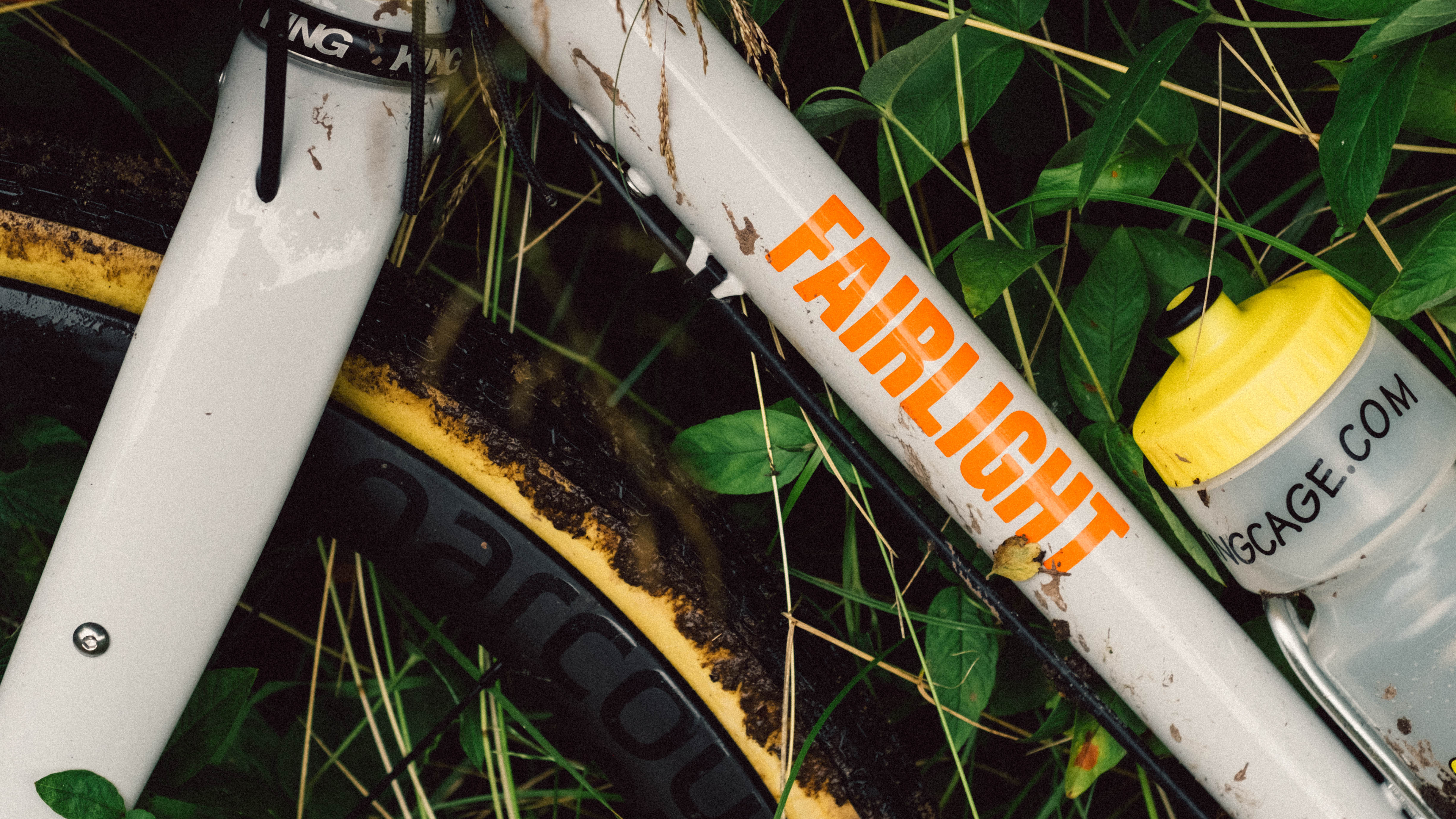 Le côté d'un vélo blanc avec des logos orange montrant des pneus tanwall boueux