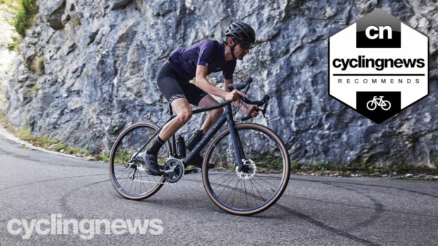 A skinny white male cyclist descends a paved hill on a Canyon Endurace, wearing black bib shorts and a purple short sleeved jersey