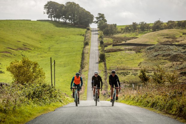 Groupe de trois cyclistes sur route montant une colline sur un chemin de campagne