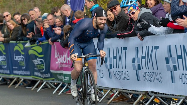 Homme faisant du vélo dur avec une expression douloureuse sur son visage, le long d'une route avec une foule l'acclamant