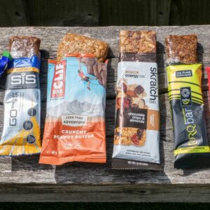 Six different energy bars on a wooden bench, each with the top open and the bar protruding out