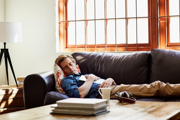 Homme adulte moyen avec tablette numérique dormant sur un canapé à la maison.