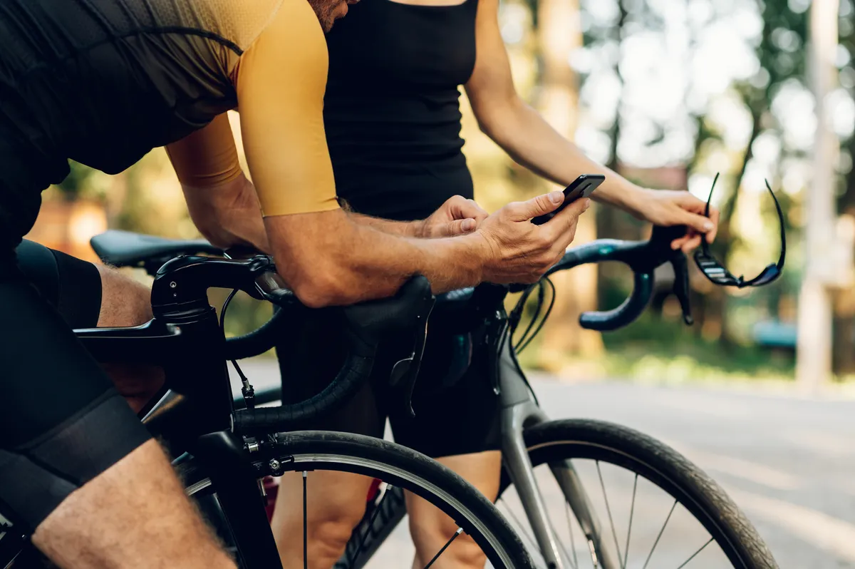 Plan recadré d'une femme et d'un homme cyclistes se détendant tout en se tenant près de leurs vélos et en utilisant un smartphone.  Activité sportive de plein air.  Jeune couple souriant à vélo.  Mode de vie sain.