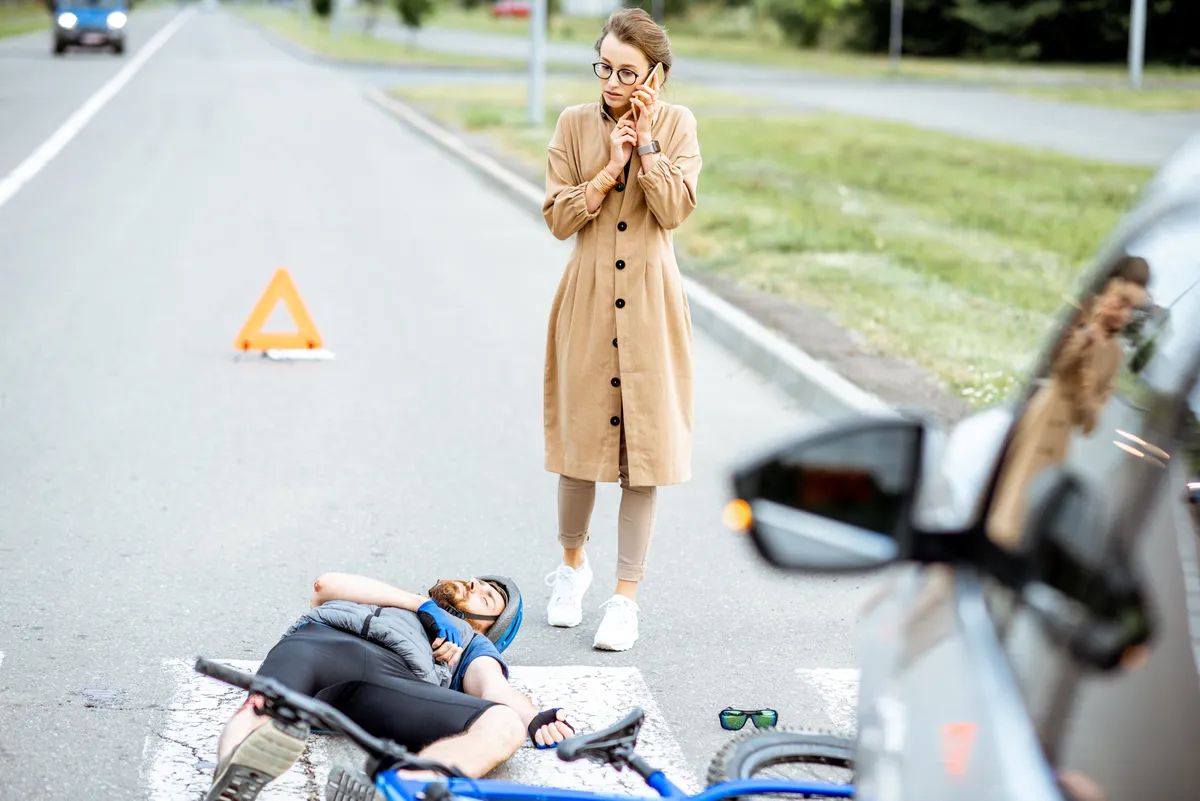 Incident de la route avec un cycliste blessé et une conductrice inquiète appelant avec son téléphone sur le passage pour piétons près du vélo et de la voiture cassés