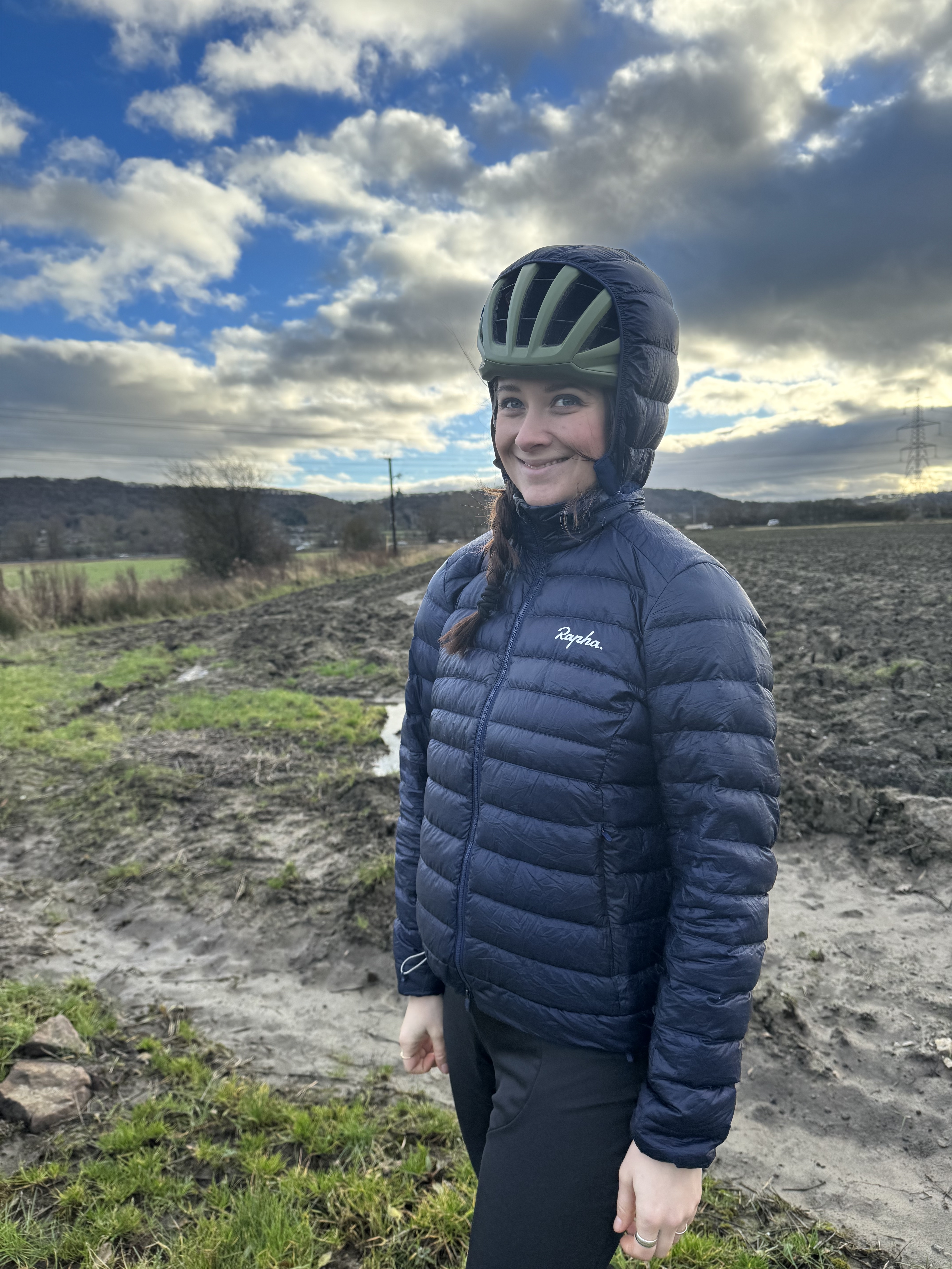 Les femmes en veste bleu marine se tiennent devant avec une capuche ouverte sur un casque vert.  Je me tenais à côté d'un champ très boueux.