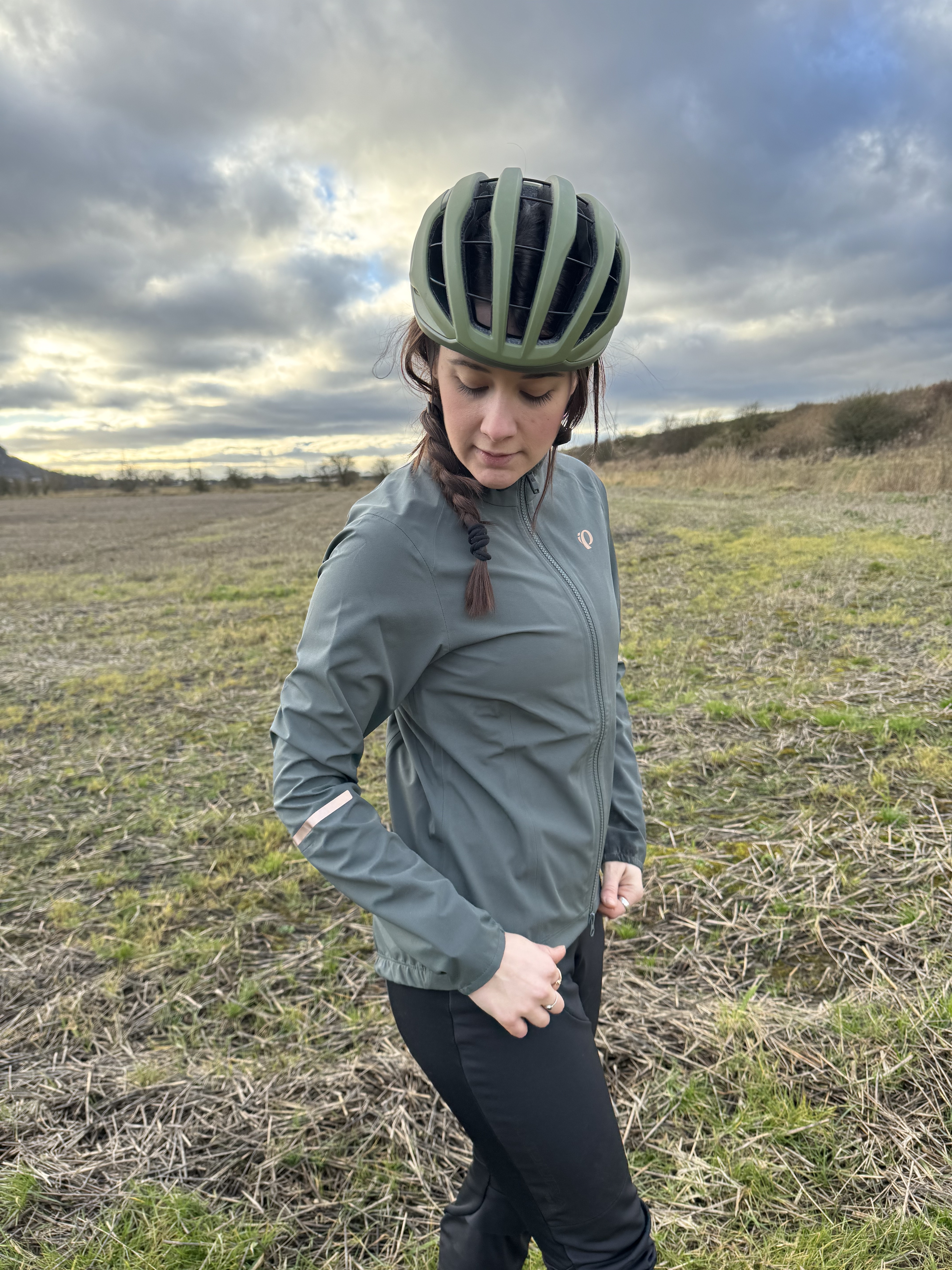 Profil latéral d'une femme en veste vert sauge portant un casque vert.  Dans un champ.