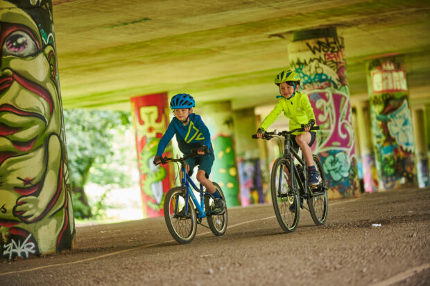 two young boys riding bikes on graffitied underpass