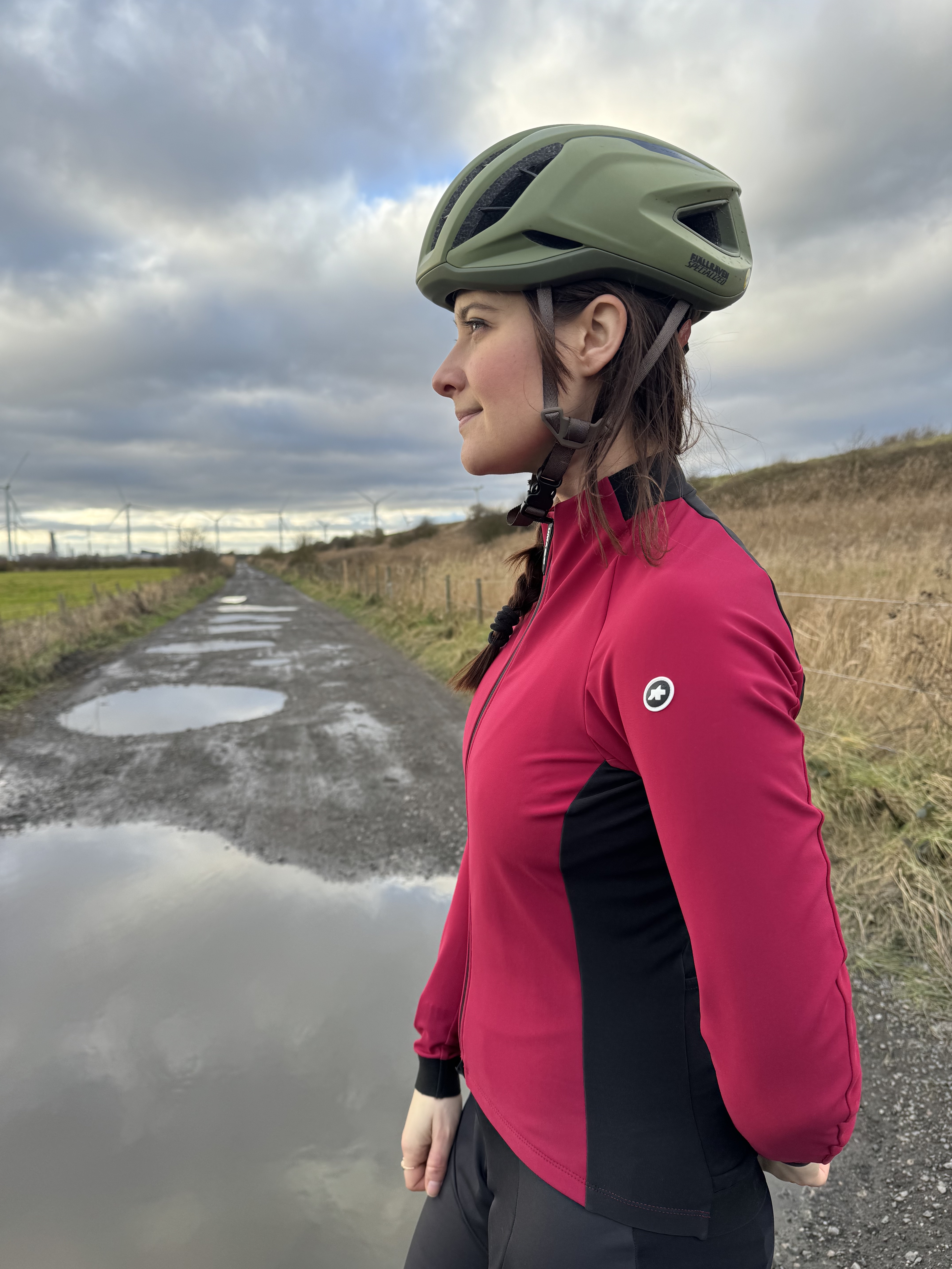 Les femmes en veste rose et noire regardent sur le côté, montrant des panneaux latéraux et des manches noirs.  Devant un champ boueux.