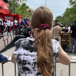 A girl stands at the barrier at a Grand Tour cycle race watching a team time trial about to start