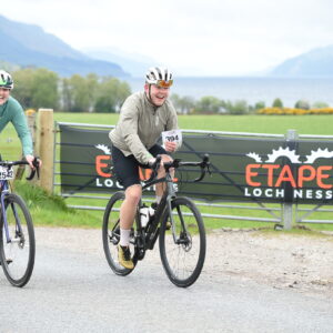 Adam Becket in a beige jacket rides along next to Katherine Moore in a