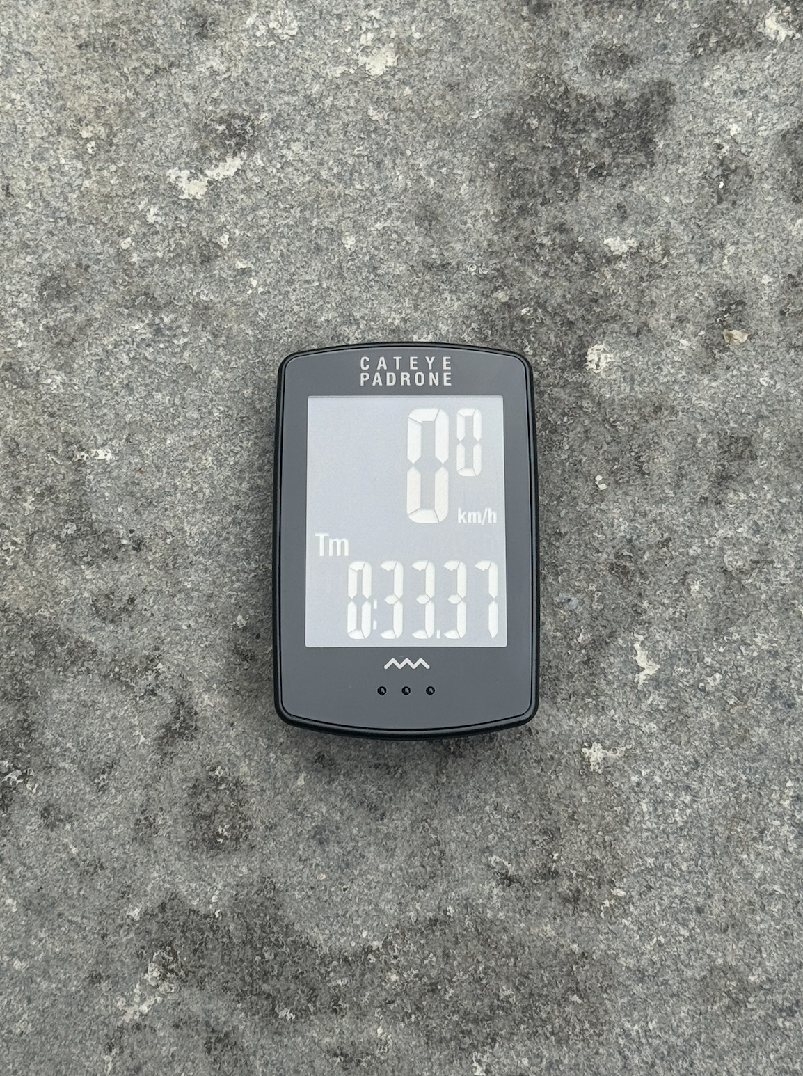 Le Cateye Padrone se trouve sur un fond gris avec l'écran illuminé et affiche KM / H et les paramètres de temps