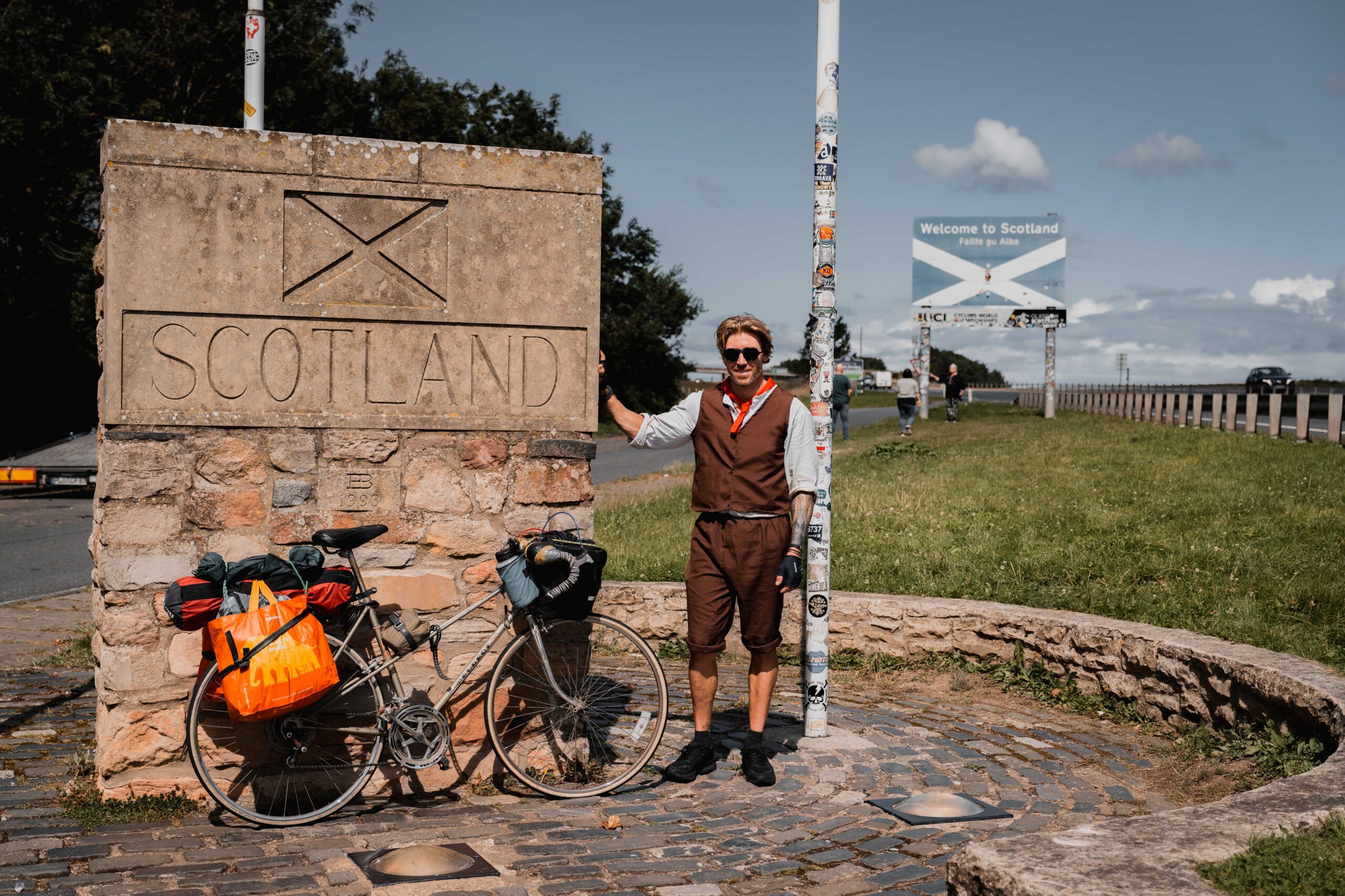 A man stands next to a sign for Scotland with his bike