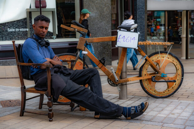A man sits next to a wooden bike