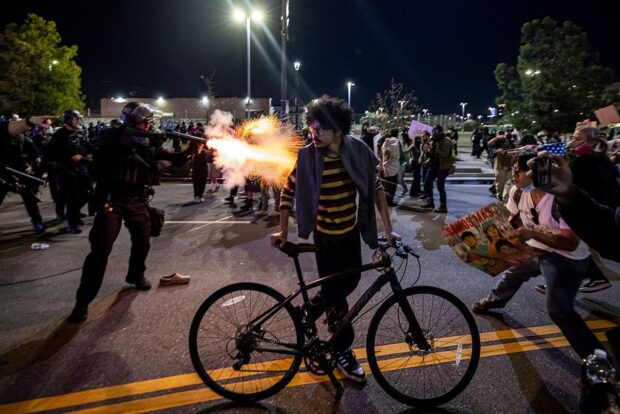 Man standing with bicycle as riot police push protesters back behind him