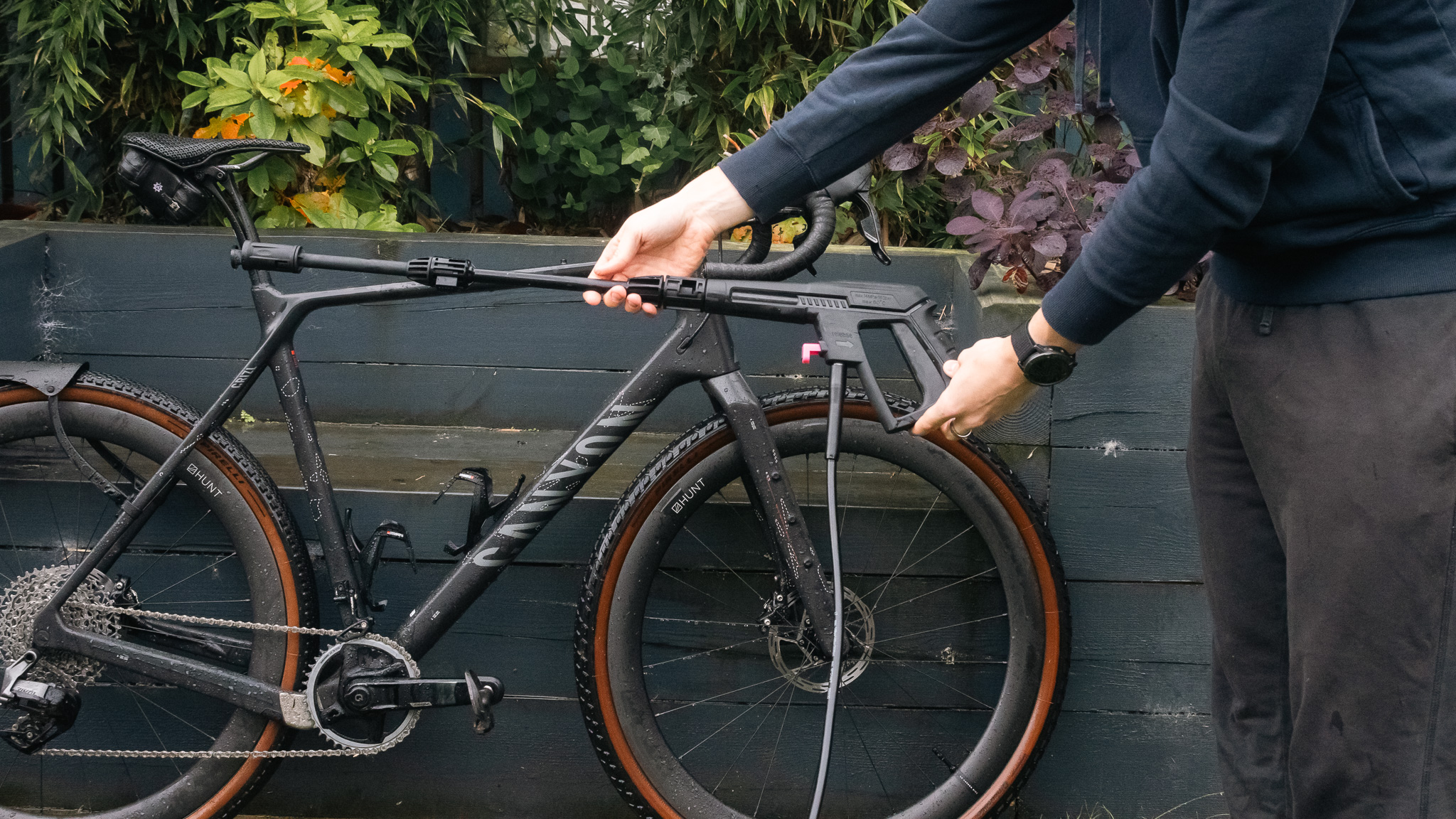 Vue de la lance du nettoyeur haute pression pour vélo mobile Muc-Off avec un vélo Canyon derrière.