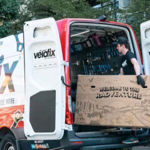 VeloFix technician carries a boxed bike into his mobile bike shop